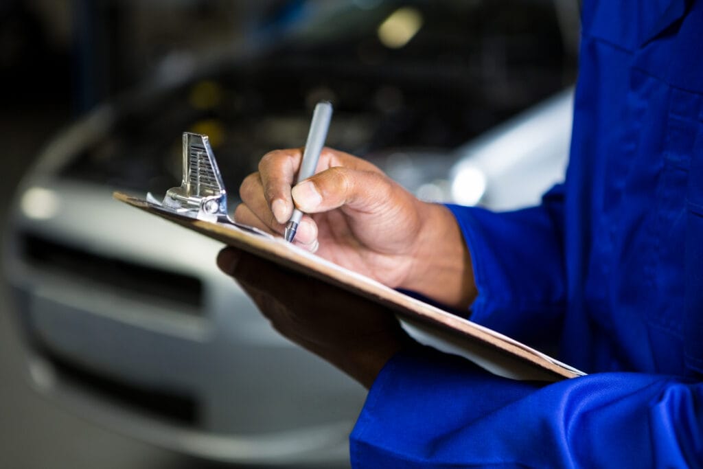 Mid section of mechanic preparing a check list at repair garage